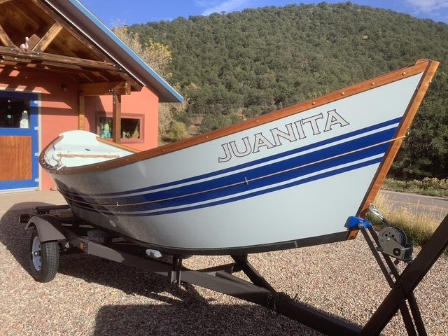 Whitewater dory made with fiberglass and resin and wood sitting in front of cabin in mountains.