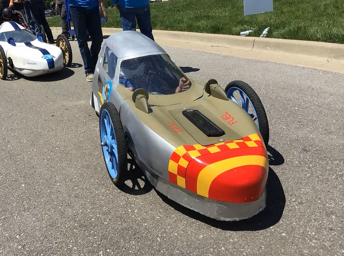 Row of white, black and blue electric cars with people in the background.