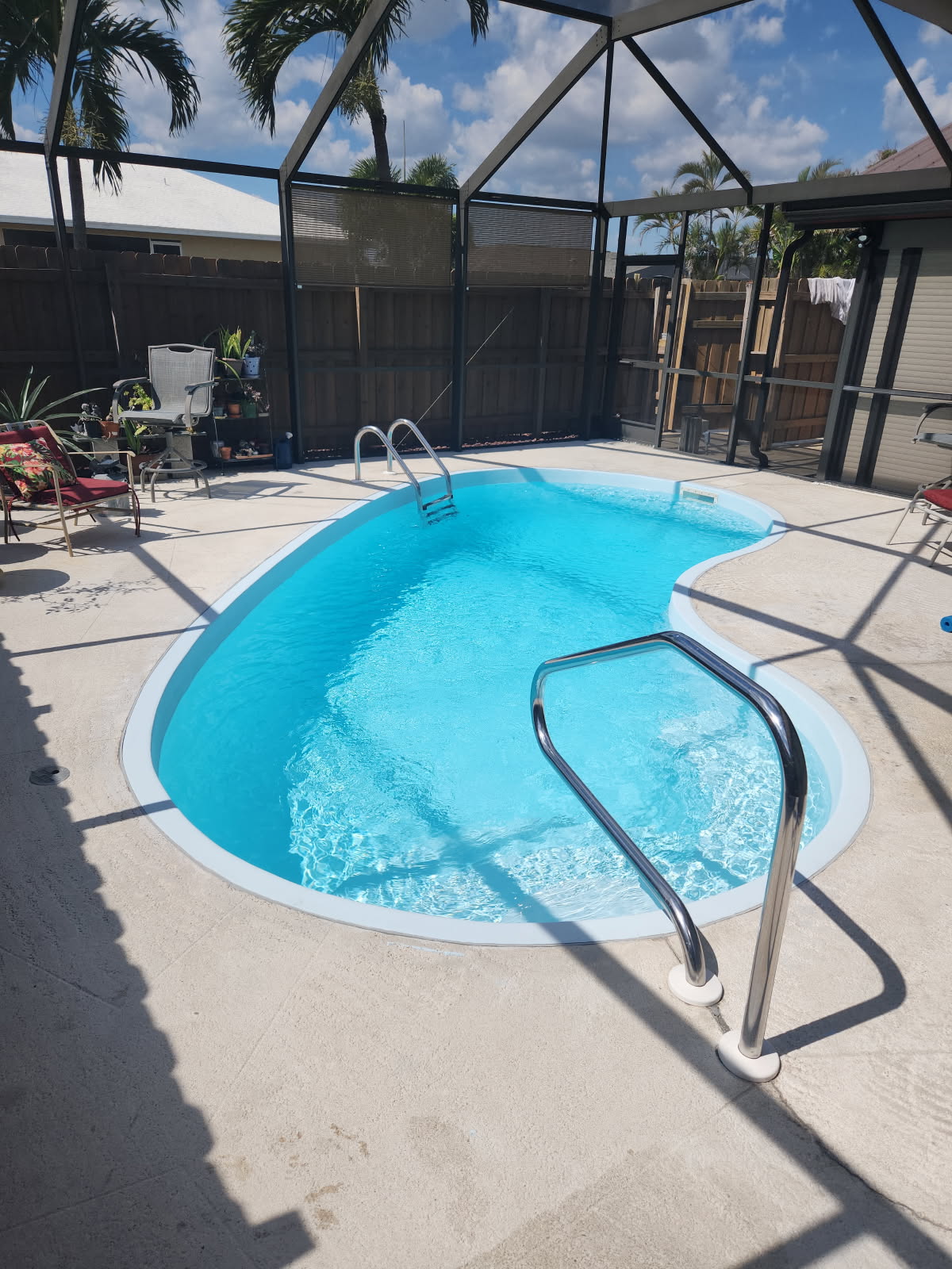 Newly resurfaced backyard pool with blue water and a few chairs surrounding the enclosed pool.