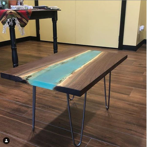 Finished epoxy resin river table made with wood and blue pigmented table top resin. Metal legs on table.