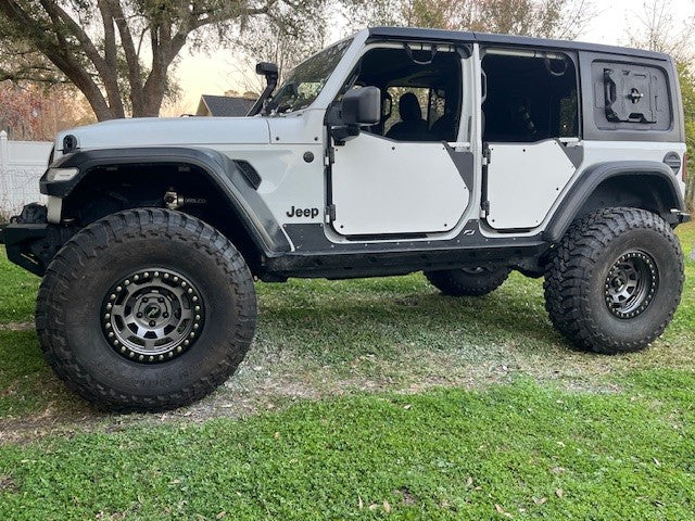 Side view of white Jeep with new fiberglass door skins sitting in grass with trees in the background.
