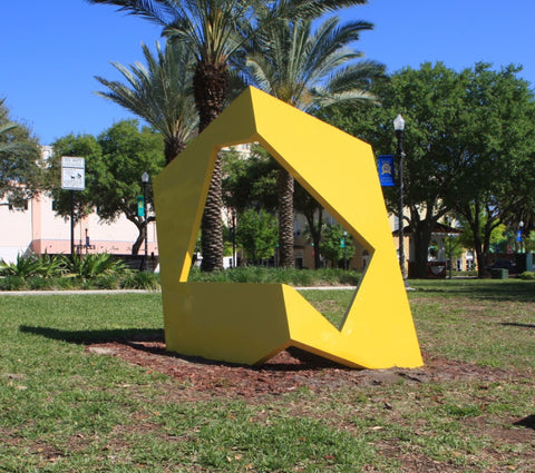 Large bright yellow fiberglass sculpture sitting in grass in front of a building.