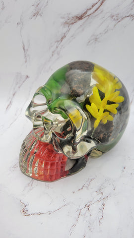 Small, clear epoxy resin skull made with rocks and red, yellow and green plants.